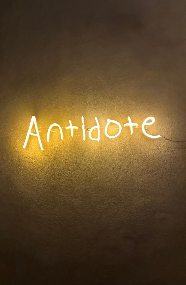 a yellow neon sign that says “antidote”