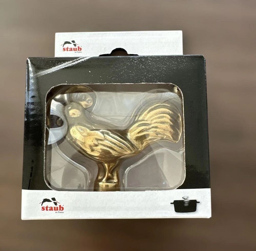 a small brass chicken in staub retail packaging. despite the name it looks golden 