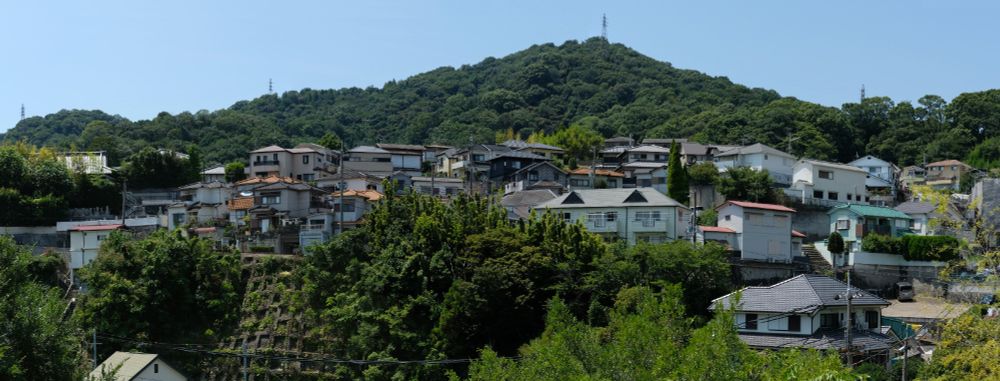 Panoramic view of a landscape in Japan with houses clustered across the mountain side.