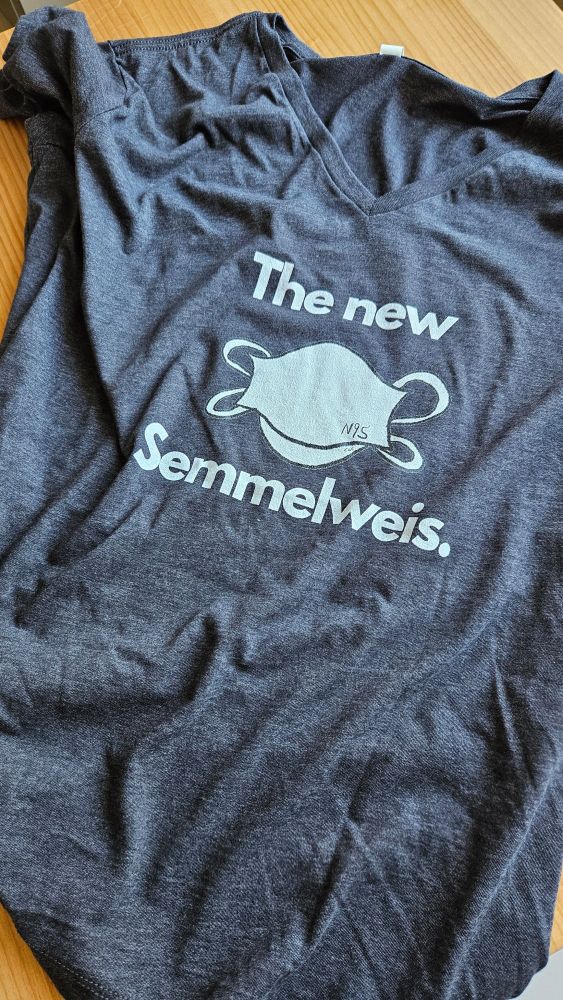 Image shows a grey v-neck tee featuring an N95 mask stating "The new Semmelweis".