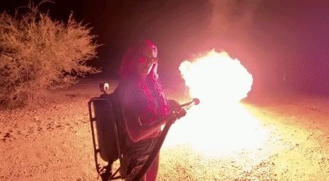 Person dressed in a red flame-retardant suit is operating a flamethrower.