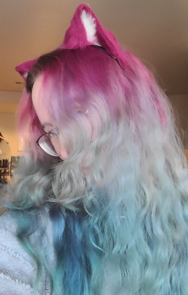 A woman wearing cat ears showing off her hair dyed in shades of red, purple, blue, and teal.