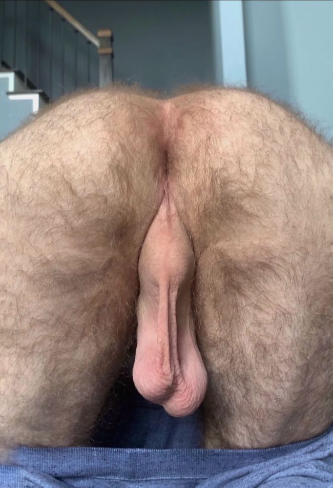 A man showing his hairy legs, butt, hole, smooth taint, and a pair of smooth low-hanging balls.