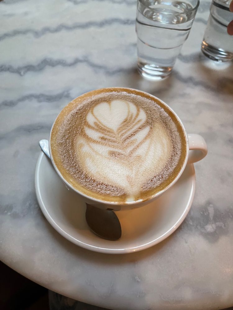 A perfect latte sits on a marble cafe table with two water glasses nearby