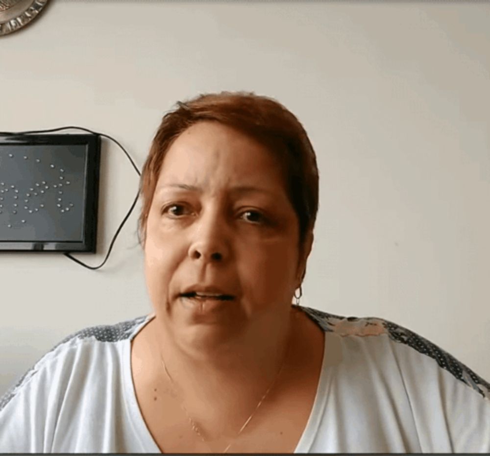 a woman in a white shirt looks at the camera with a picture on the wall behind her