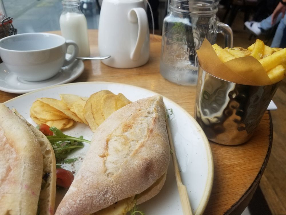 A sourdough sandwich, tea, eater and some chips on a round table. 