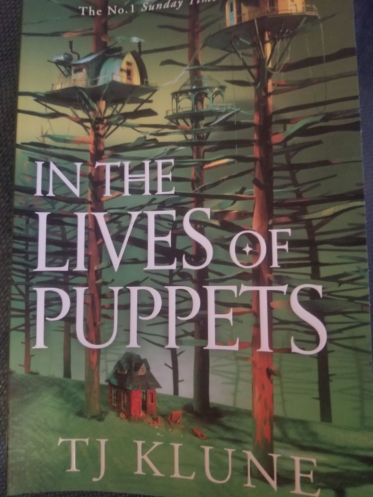 Cover of In the lives of Puppets by TJ Klune. Picture of a forest with tree houses. 