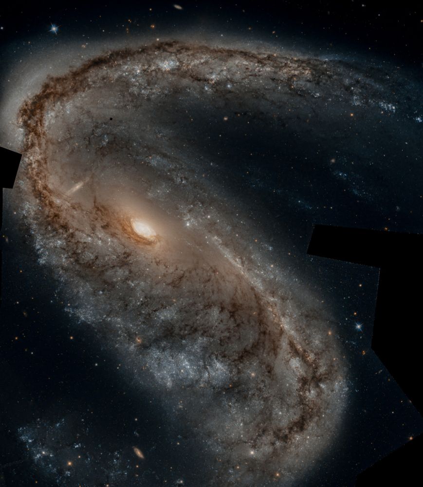 A spiral galaxy with two arms: one stretching to the top right of the image, the second to the bottom left. The arms appear orange/red. The centre is really bright. A lot of background galaxies can be spotted everywhere, with one of them appearing like a ghost behind the main galaxy of this image! 