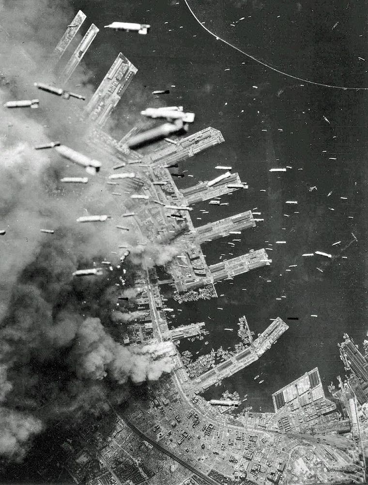 Incendiary bombs are dropped over the city of Kobe, Japan from American B-29 Superfortresses, as the landing piers and buildings of the city are burning below, 4 Jun 1945 (USAAF Photographer), Public Domain