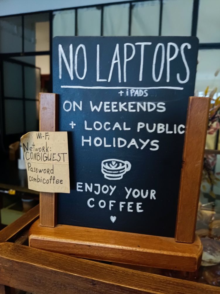 A handwritten blackboard sign on the counter of Combi Coffee Roasters in Porto, the sign reads "No laptops + ipads on weekends + local public holidays. Enjoy your coffee." 