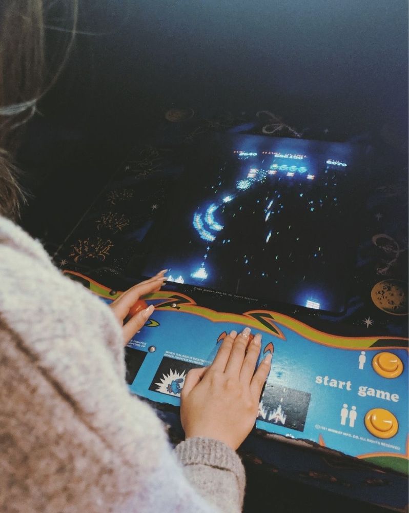 A girl playing Galaga at the arcade, joystick in hand, as the screen lights up with alien ships