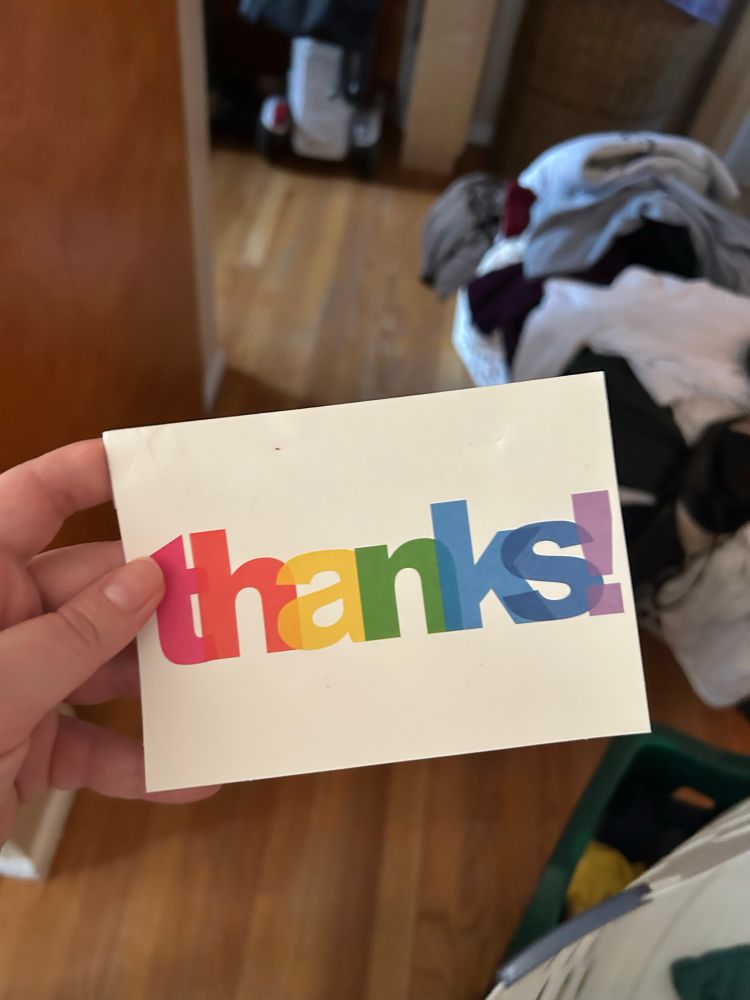 A hand holds a white card that says “thanks!” in rainbow letters