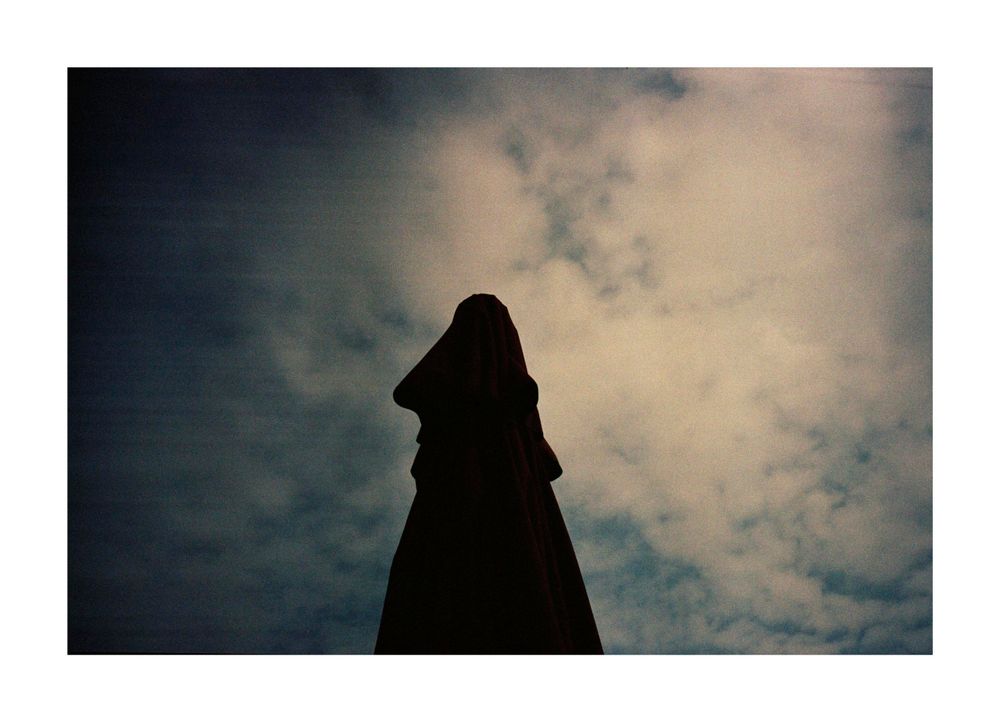En el fondo un cielo con nubes. En primer plano una forma o silueta confusa en contrapicado y contraluz.