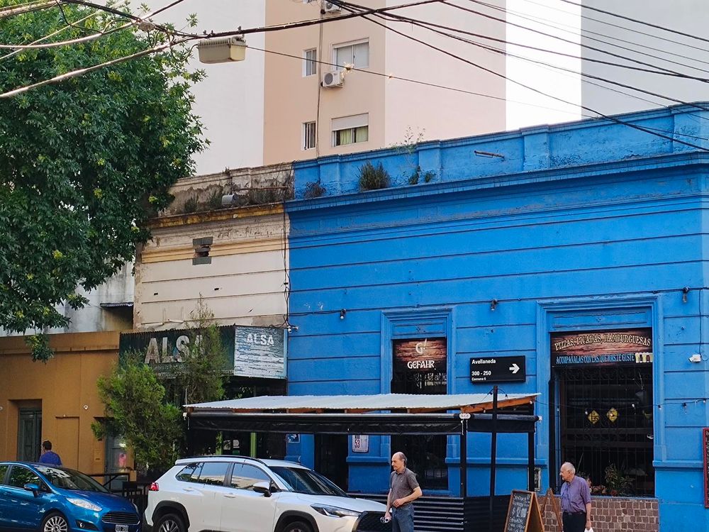 low building, right half (err, two-thirds) is painted bright blue and has a restaurant, the left part has a sign that says ALSA in big letters. two cars parked in front.