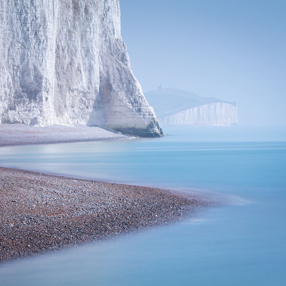A square photograph of the Seven Sisters, chalk cliffs in East Sussex, UK, with Belle Tout lighthouse in the background. 
