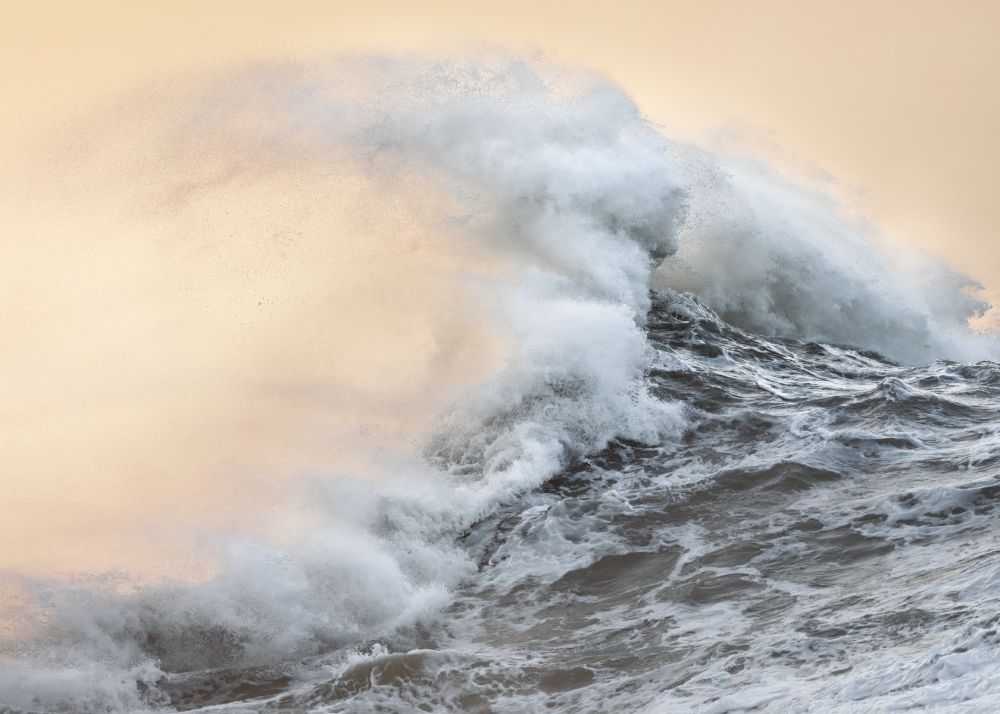 A fast-shutter photograph of a curling wave in front of an apricot sky. Taken at sunrise. East Sussex, UK. 