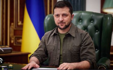 Image of Volodymyr Zelensky sitting at desk with Ukrainian flag to his right