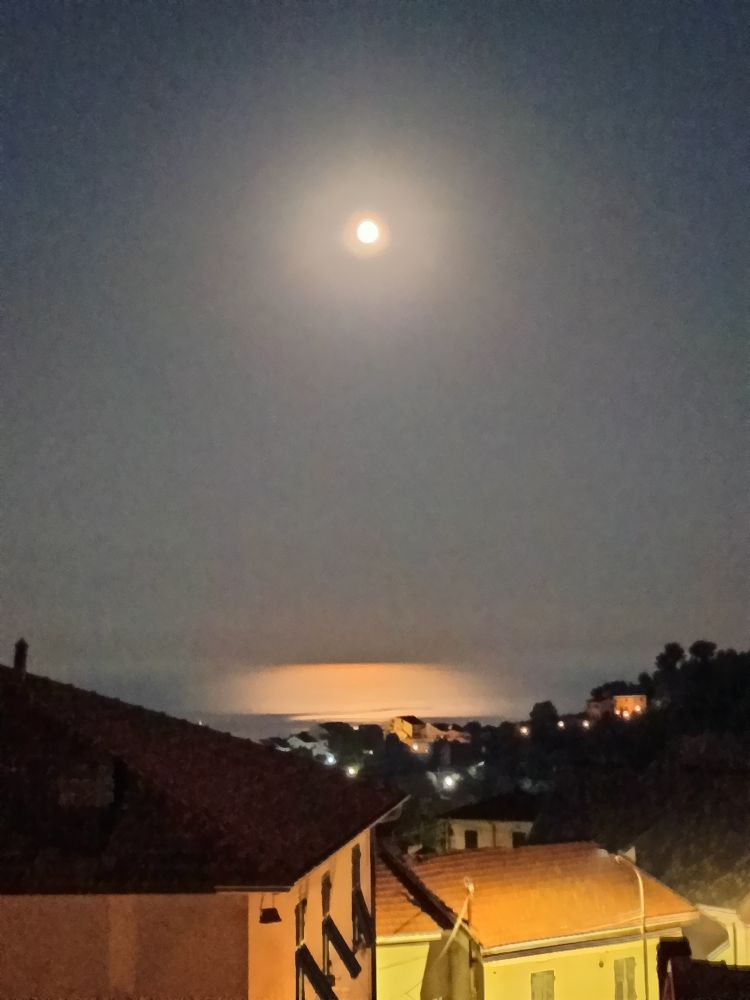 Red moon and its reflection on the Mediterranean Sea, some houses. 
