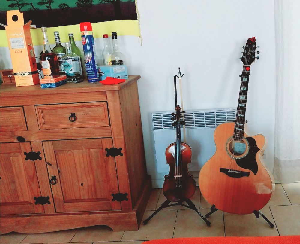 What might be generously termed a "still life" if one were being very kind. 
A picture showing part of asideboard with some bottles on it; on stands, upon the ceramic tiled floor, next to the sideboard are a violin and an acoustic guitar.