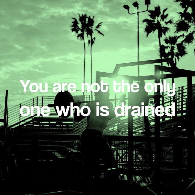Text: You are not the only one who is drained

Image shows a person doing barbell squats in front of some bleachers and palm trees.