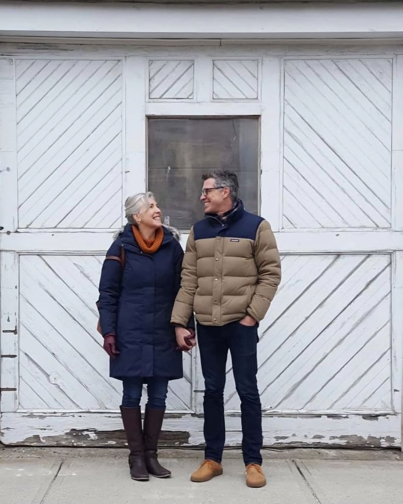 Sandi and Jim standing in front of an old wooden garage door, looking at each other and smiling. 