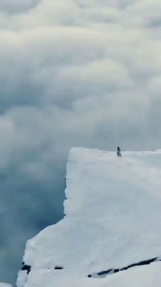 a person is standing on the edge of a snow covered mountain