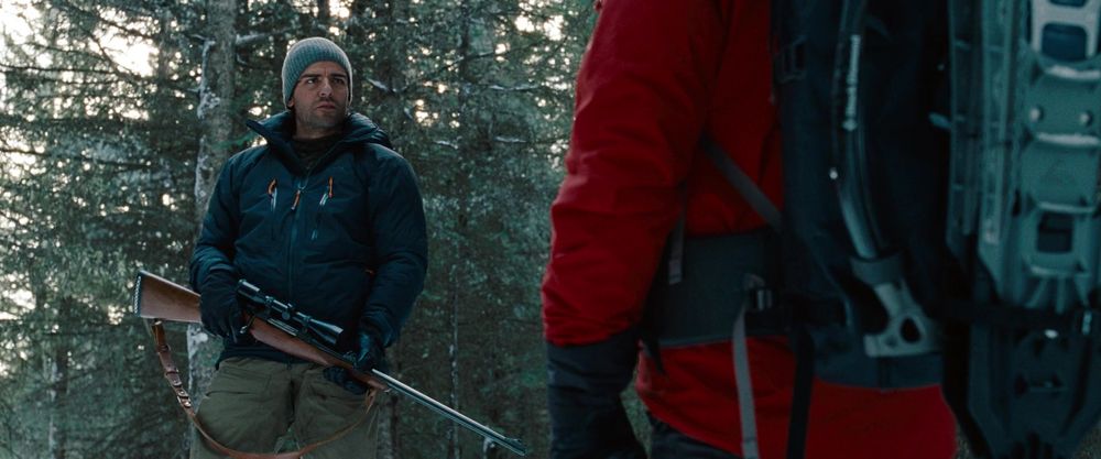 "Outcome #3," portrayed by Oscar Isaac, holding a hunting rifle with a scope on a snowy, tree-lined ridge. 