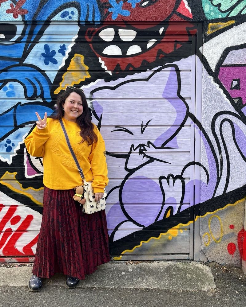 A girl in a yellow jumper standing next to graffiti of the Pokémon mew