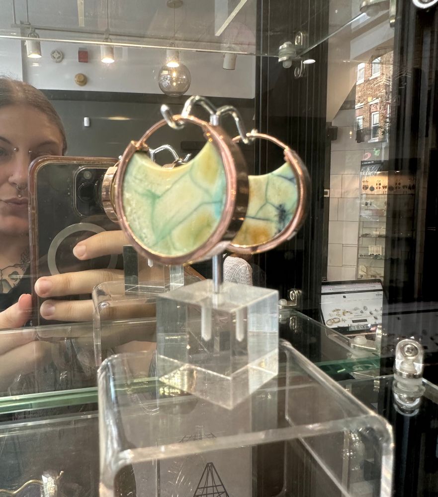 A pair of beautiful green/yellow/blue circular ear weights on a clear plastic display; you can see my face in the reflection but that’s not important 