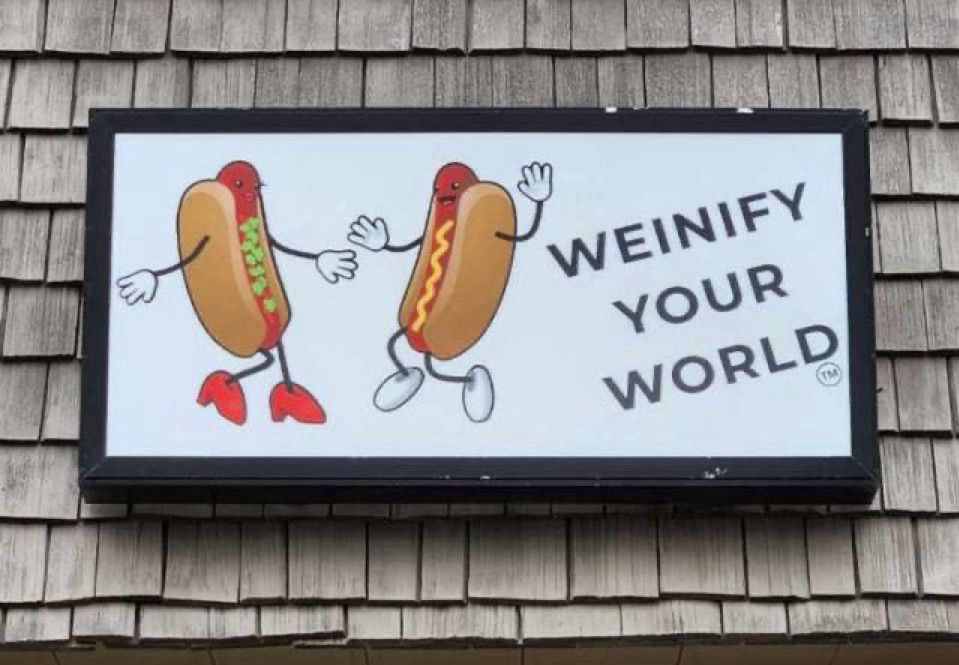 A sign on a roof with two dancing hot dogs and the slogan “Weinify Your World.”