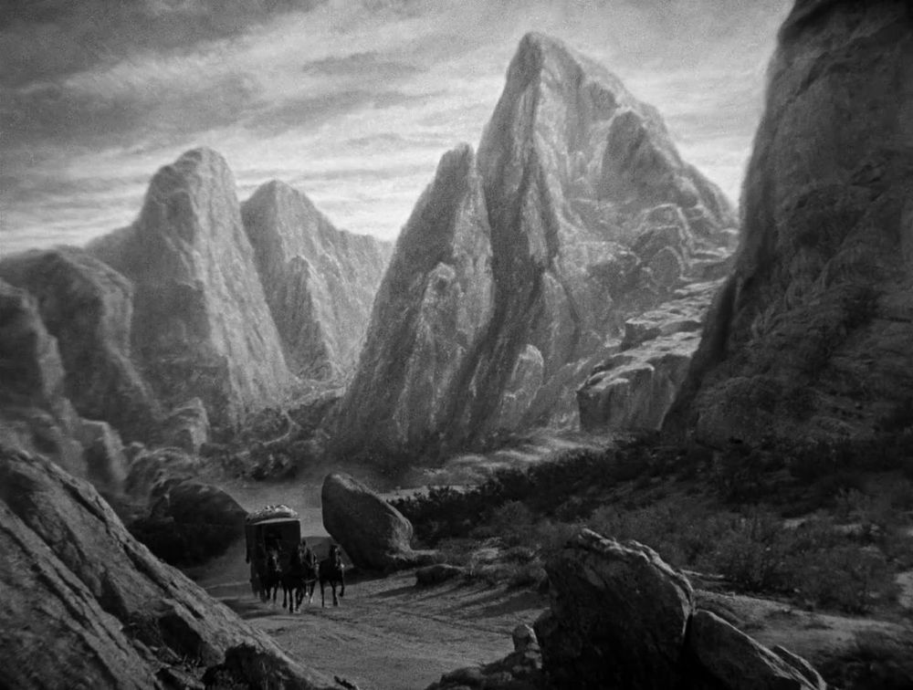 A still from Dracula (1931, Tod Browning). A matte painting of the jagged, craggy peaks of Borgo Pass dominate a live action carriage on a winding road at the bottom of the frame. 