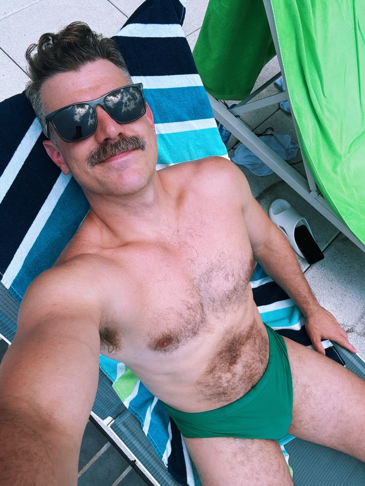 PT in a green speedo lounging by the pool 