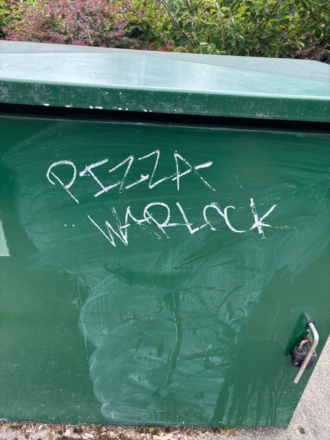 A bit of white graffiti on a green background saying Pizza Warlock