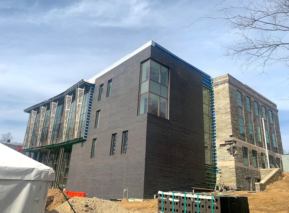 Three-quarters view of a building under construction, showing a new brick section added onto the old part of the building.