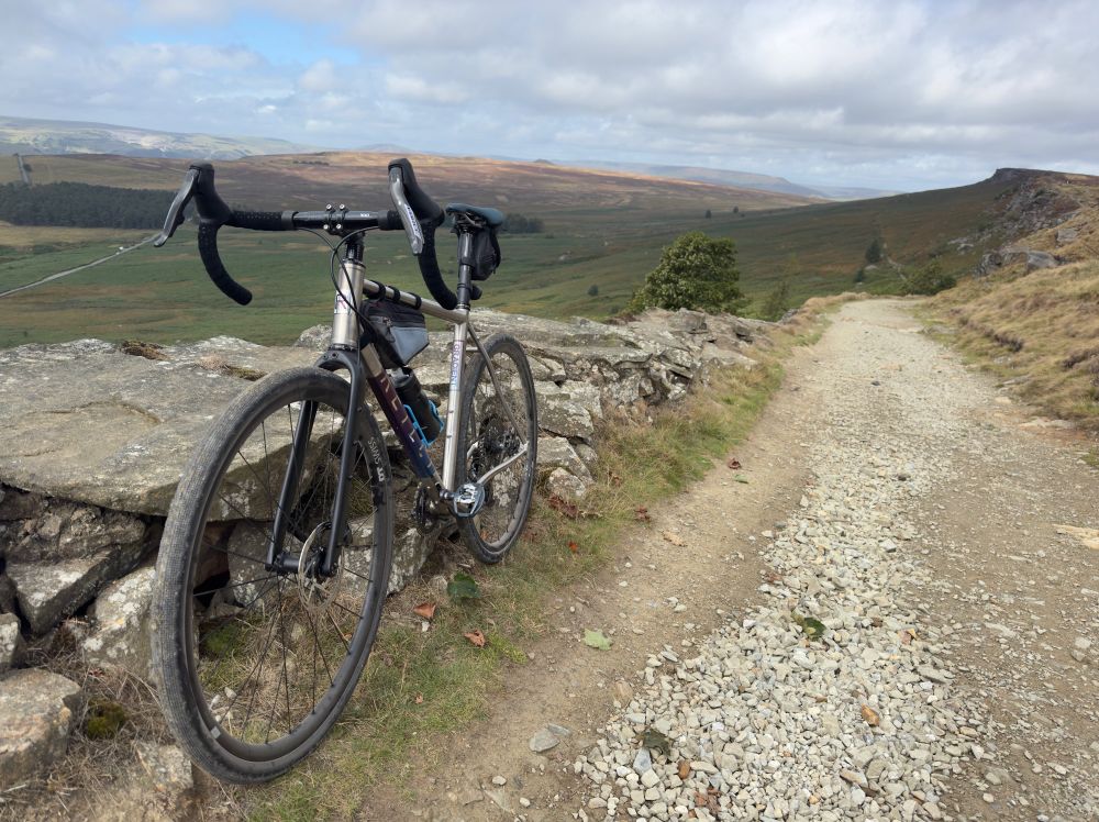 A gravel bike propped up against a wall on the Long Causeway in the Peak District National Park - a glacial valley overlooked by the Stanage Edge escarpment