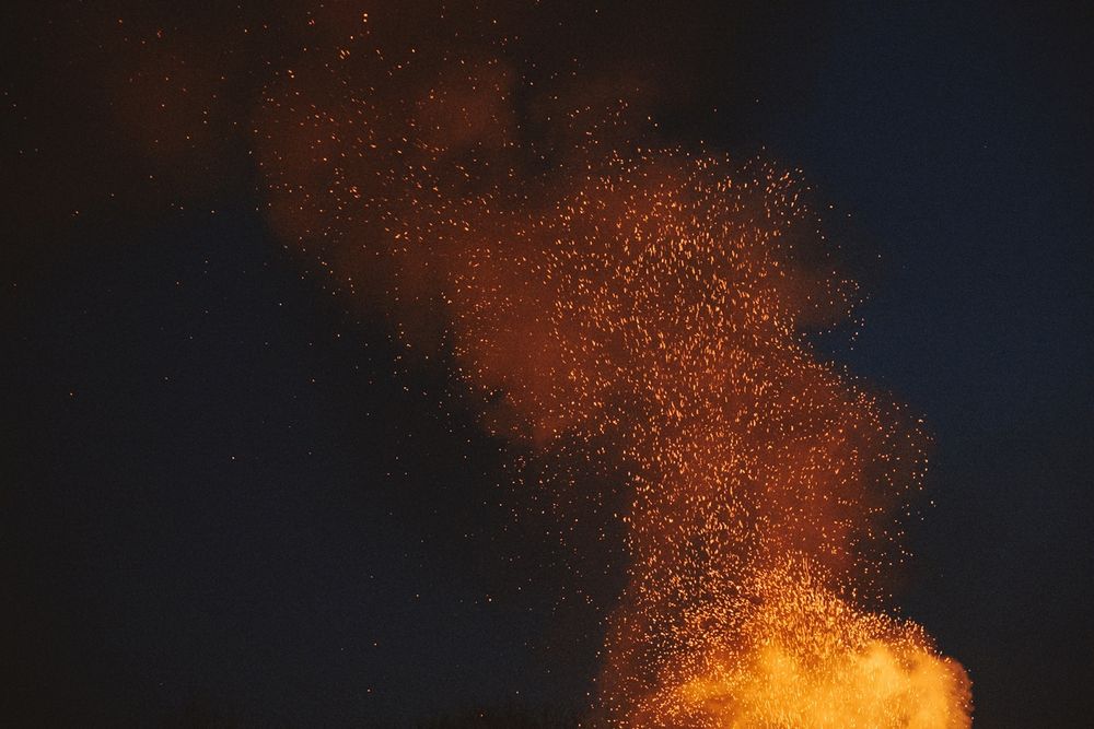 Funkenflug aus einem Lagerfeuer bei Nacht. Von unten rechts nach oben links fliegen die Funken vor dem Nachthimmel in Wolken.