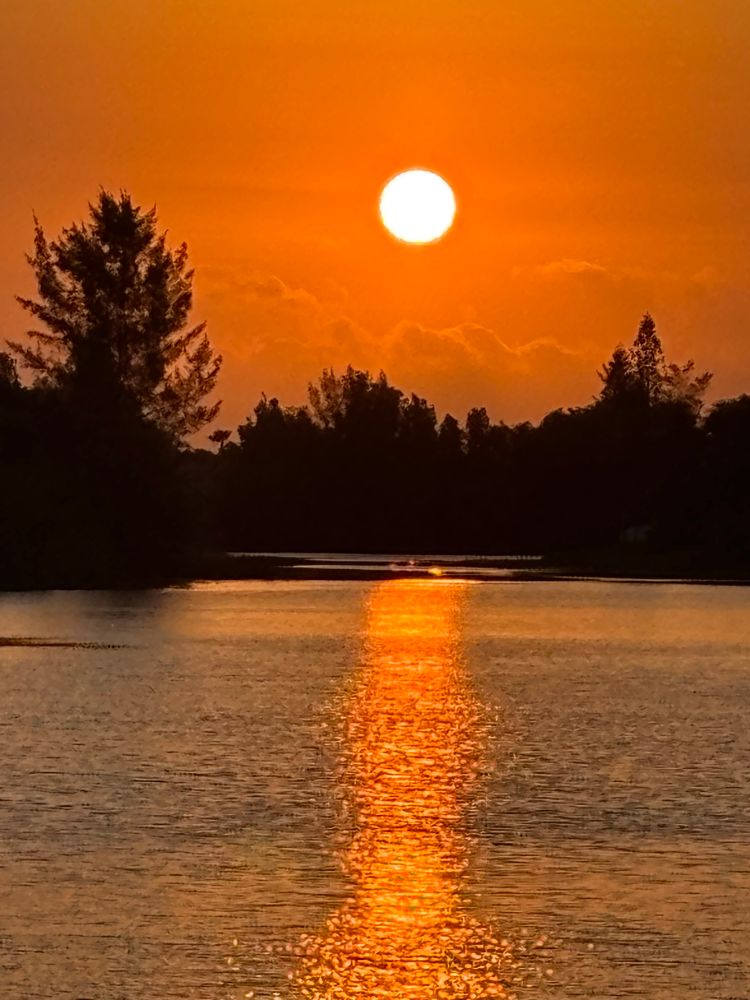 Morning sunrise over the lake, orange colors in the water and sky, trees and clouds in the background 