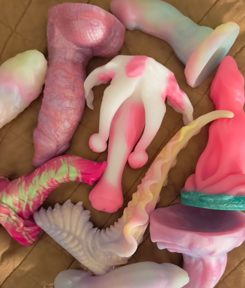 An assortment of pink-forward fantasy toys spread on a mustard colored bed quilt