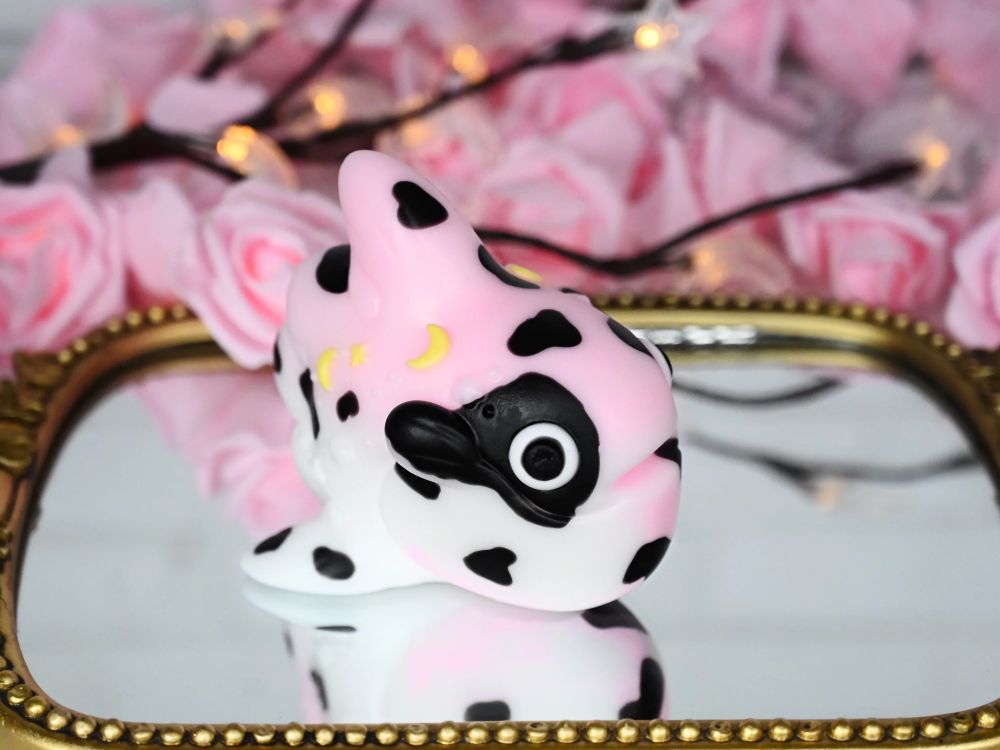 Large pink and white CC glub with black cow print and yellow star and moon inclusions, sitting on a golden mirror