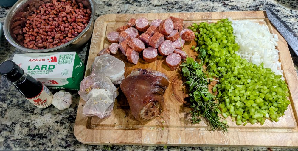 A bowl of soaked beans next to a cutting board with the NOLA trinity and various cured meats