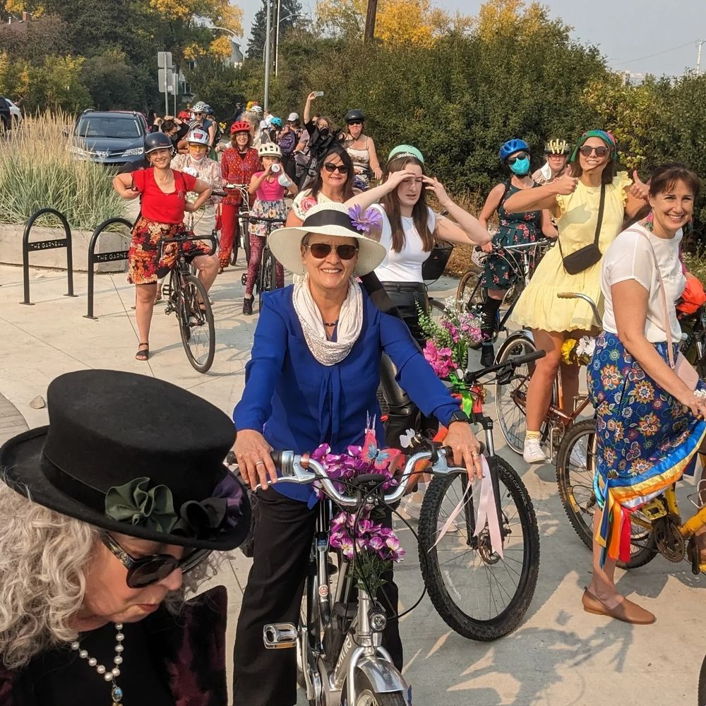 Daytime; women dressed in fancy styles ride bicycles in Edmonton.
