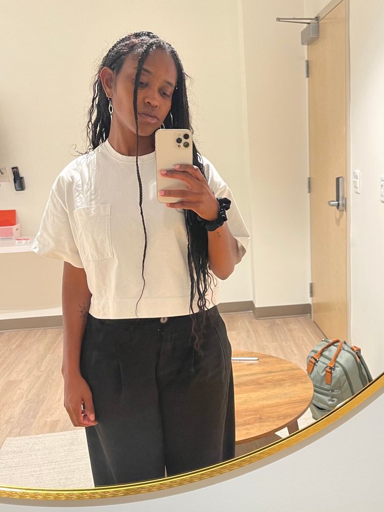 Mirror selfie of user wearing a white shirt and black pants. They have loose, curly braids. 