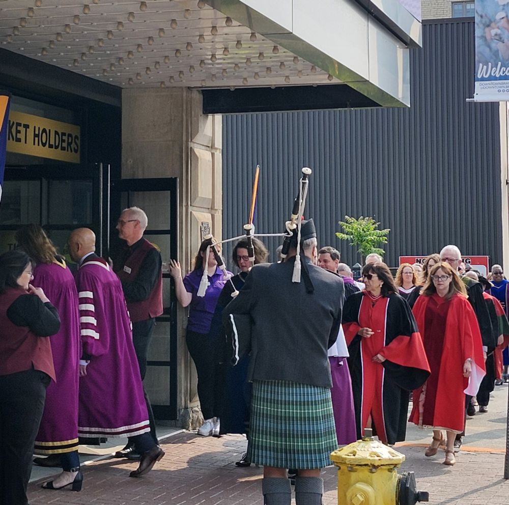 A procession of University graduates, faculty and administrators going into a theatre. 