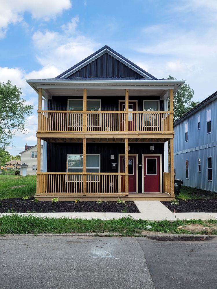 Black-sided duplex with a two-story porch and red doors