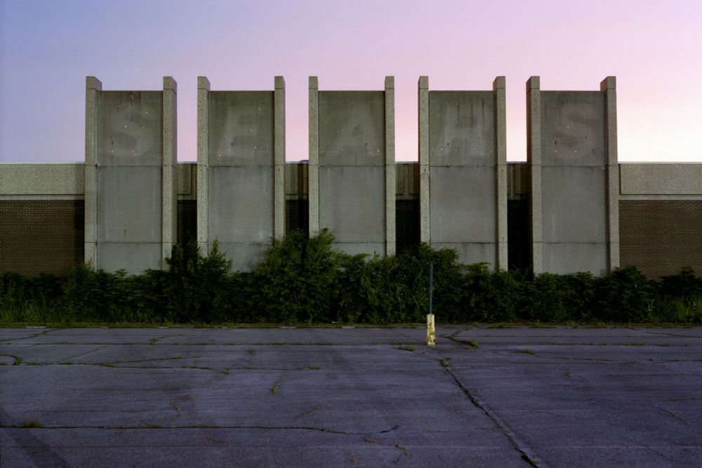 Photograph. An abandoned Sears department store at twilight, the labelscar of the SEARS letters is visible on five concrete columns separated from a brick building, behind.

Sears, Salem Mall
Trotwood, Ohio