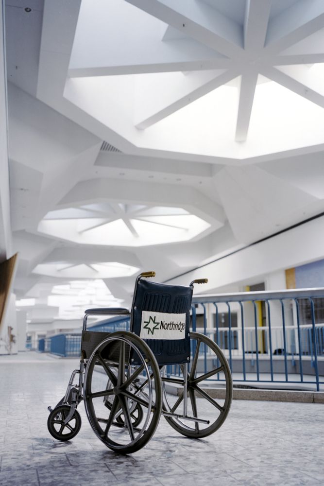 Photograph. A wheelchair in an abandoned shopping mall; large skylights loom overhead.
