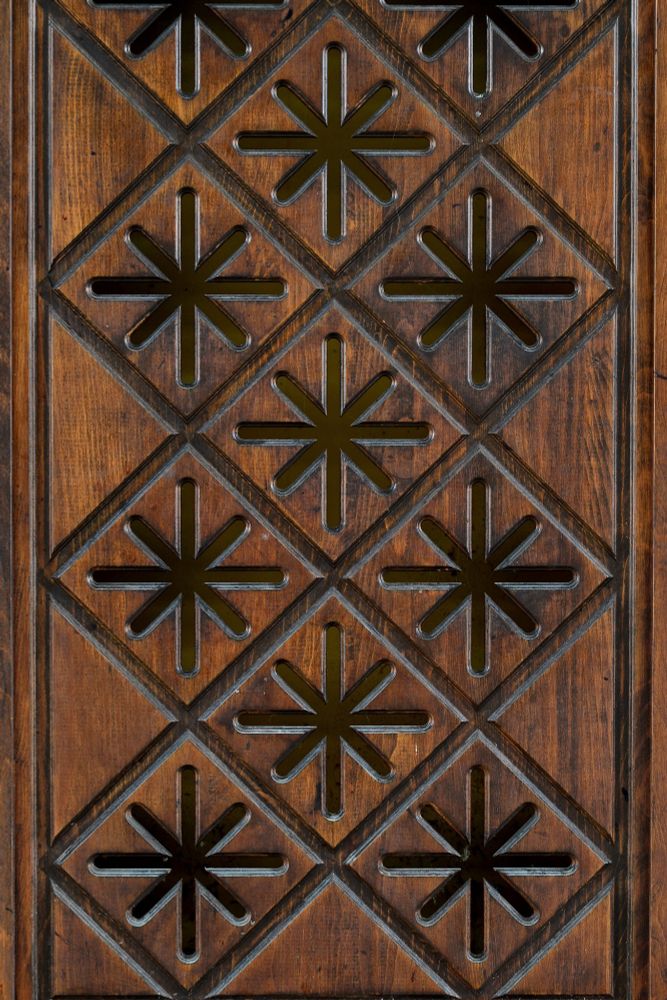 Photograph. Details of wood facade paneling, a pattern of diamond carvings and star-shaped cutouts revealing a yellow background. The star-shaped openings would be backlit with fluorescent lighting.