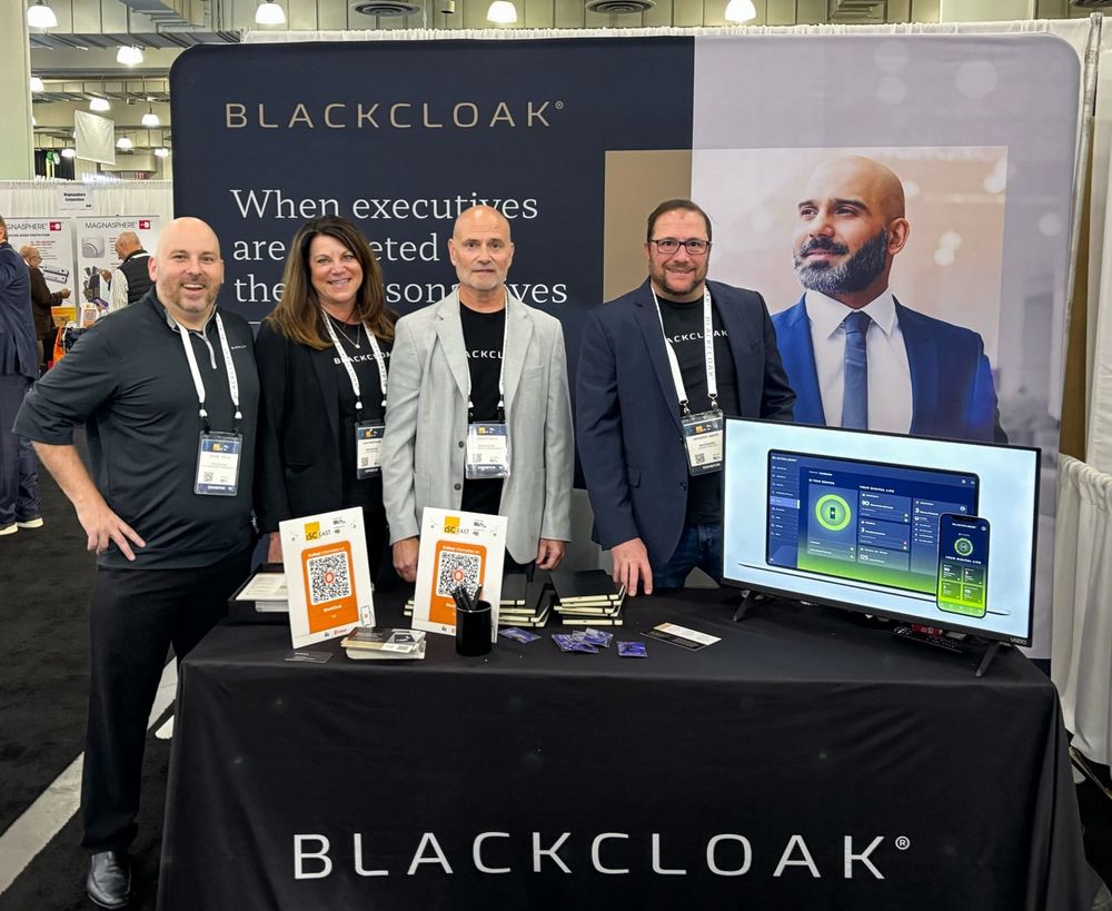 Four individuals standing in front of a BlackCloak promotional booth at a tech event.