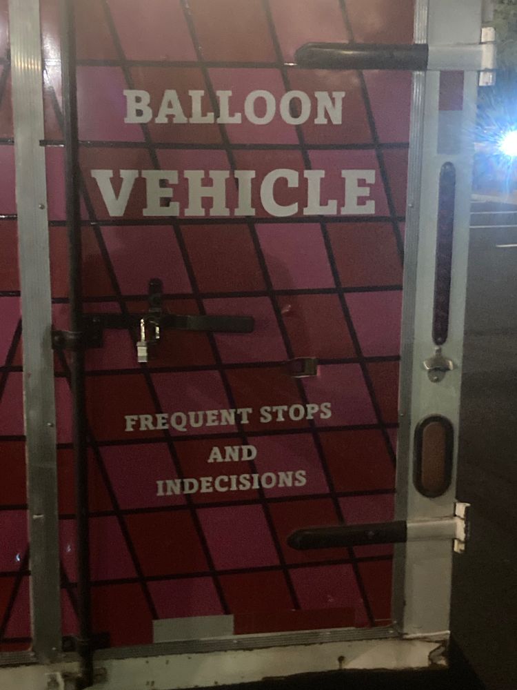 Back door of a balloon chasing vehicle with the phrase “Balloon vehicle: frequent stops and indecisions”
