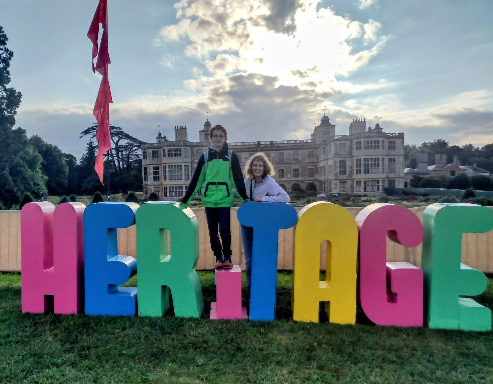 Historic house backdrop. Two people in foreground with large letters spelling heritage.